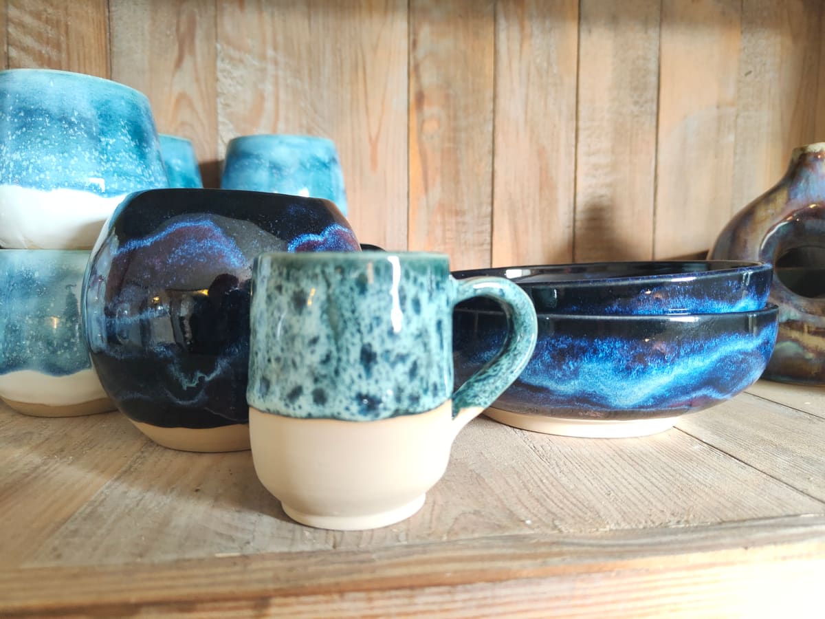 Blaue und gesprenkelte Becher auf einem Holzregal im Atelier